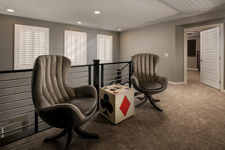 A white window treatment on a darker wall can do wonders for your Destin home. two chairs and a small dice-themed table in front of a stairwell with shuttered covered small windows
